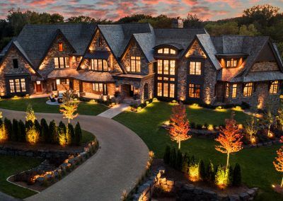 an aerial view of a luxury home at dusk with lights on the windows and landscaping