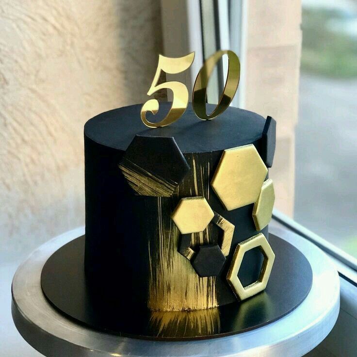 a black and gold birthday cake with five golden numbers on it's top, sitting in front of a window