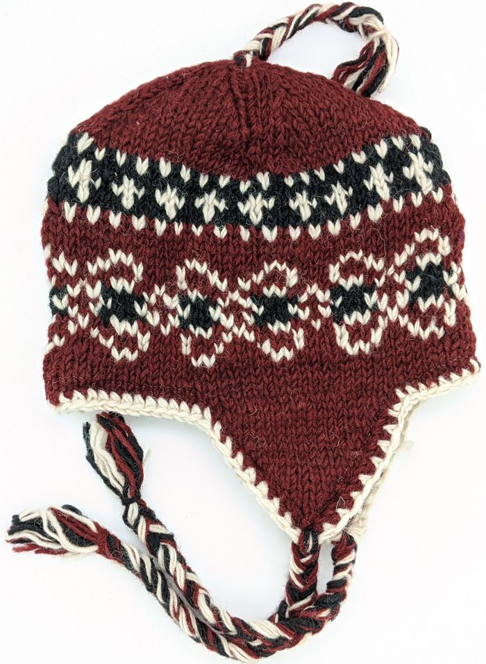 This is a pure wool hand-knit hat - in rust red, black, white - with ear flaps and top and side tassels. This winter/ski hat has a fleece lining and One size fits most but can be snug on a large head. The hat is designed for the outdoors, for the cold and windy conditions, including your ski trips. Or just wear it anytime to stay warm and cozy. Traditional Beanie Hats For Winter, Traditional Beanie For Winter, Red Wool Winter Hat, Winter Crochet Hat With Ear Flaps, Burgundy Brimmed Winter Hat, Hand Knitted Winter Hats With Ear Flaps, Winter Hand Knitted Hats With Ear Flaps, Traditional Brown Winter Hat, Traditional Winter Hats With Ear Flaps