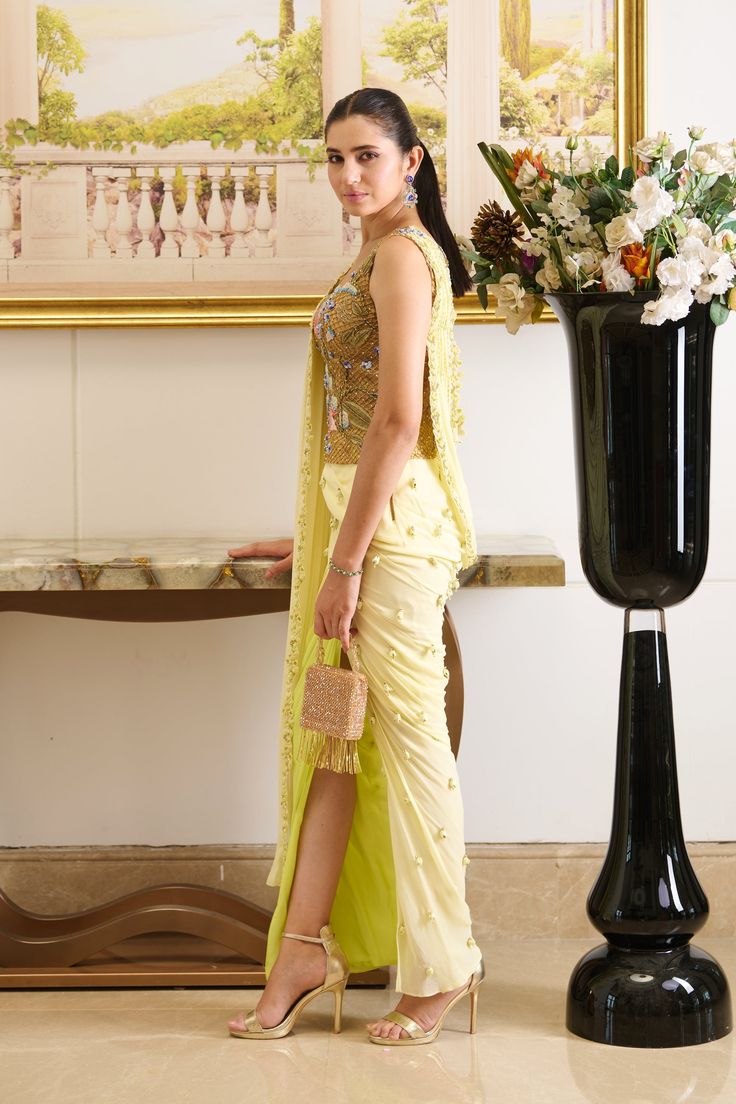 Rhyming perfectly with your day-time soirees, Lulu is a pre-stitched saree featuring a golden-hued designer blouse made out of fish-net fabric with floral embroidery detailing and a front pallu. The innovative draping style creates an exquisite piece immersed in the complimentary palette of lemon, presenting a fresh look for seasonal affairs. A perfect amalgamation of modernity and sophistication indulged in the traditional silhouette is a must-have festive essential that your wardrobe has been missing out on. Sleeveless blouse crafted out of fish-net fabric and adorned with beautiful floral embroidery detailing. The pre-draped skirt featuring a slit is adorned with dainty detailing of embroidered drops. Front pallu embellished with a linear sequined pattern and floral cut-work detailing a Sleeveless Pre-draped Saree With Resham Embroidery For Party, Resham Embroidery Saree With Side Open, Festive Dress With Sheer Dupatta And Side Open, Party Side Open Pre-draped Saree With Resham Embroidery, Reception Choli With Zari Work And Front Open, Front Open Choli With Zari Work For Reception, Gold Pre-draped Saree With Resham Embroidery For Evening, Side Open Pre-draped Saree With Resham Embroidery For Parties, Traditional Sleeveless Sharara For Evening