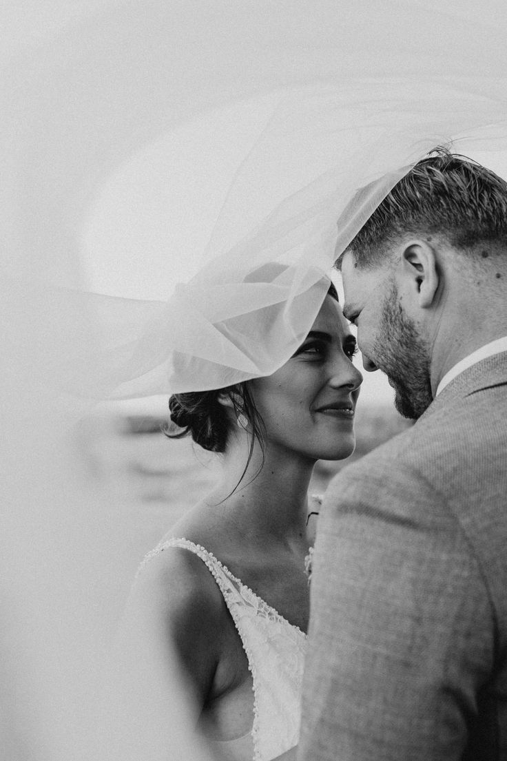 black and white photograph of a bride and groom looking at each other with veil over their heads