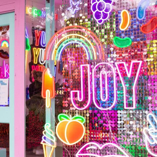 a store front window with neon signs and fruit on the windows display it's bright colors