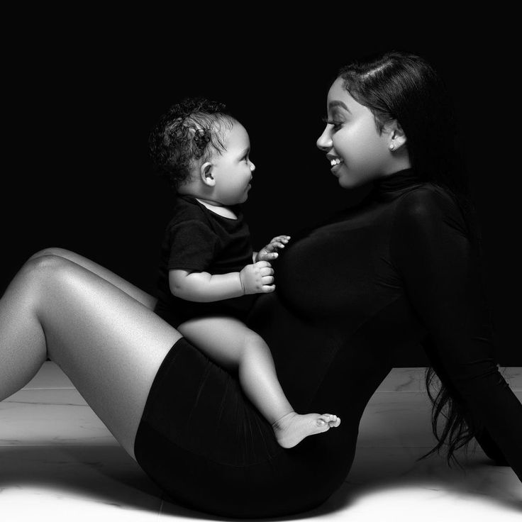 a black and white photo of a woman holding a baby in her lap while sitting on the floor