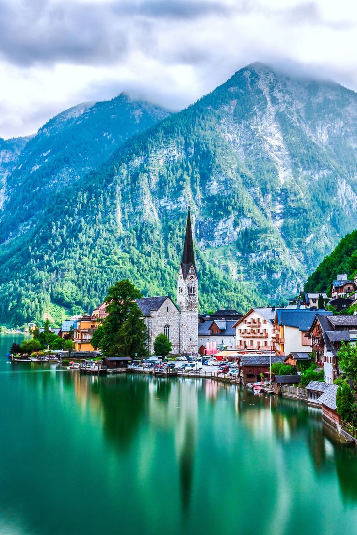 a lake with mountains in the background and houses on the shore, surrounded by greenery