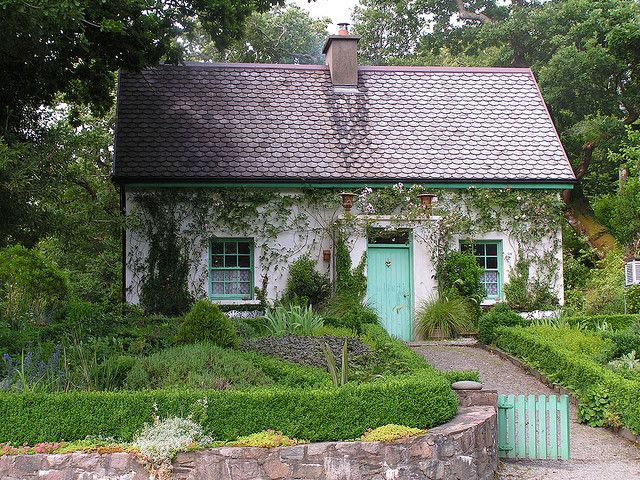 a small house with a green door surrounded by greenery and bushes in front of it