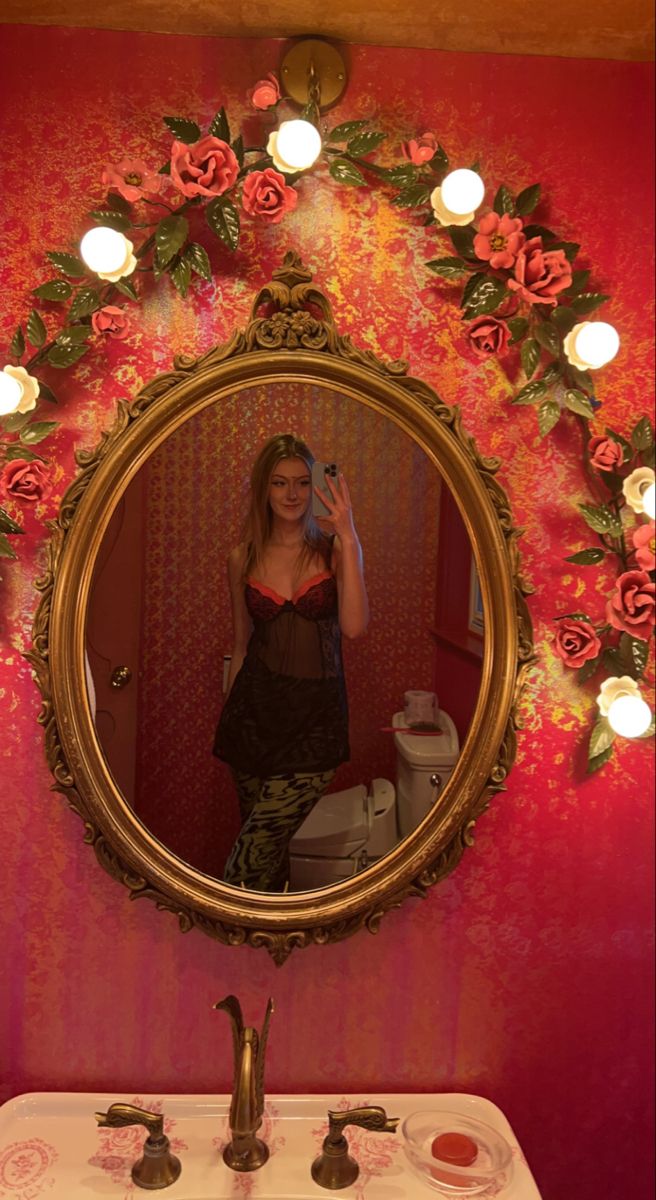 a woman taking a selfie in front of a mirror with flowers on the wall