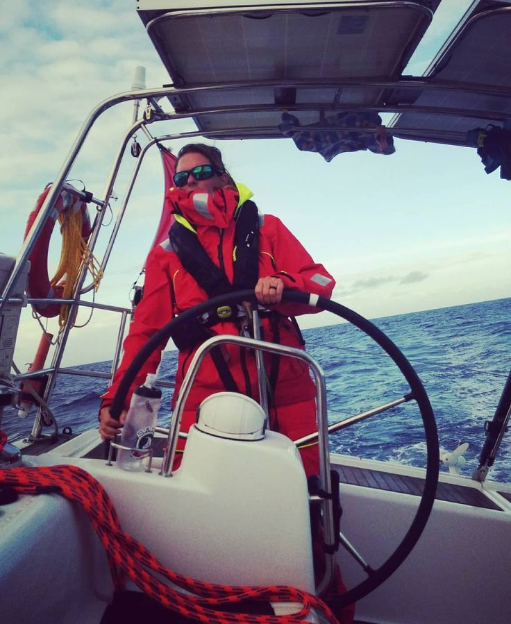 a man in red is standing on the front of a boat with his arms around the steering wheel