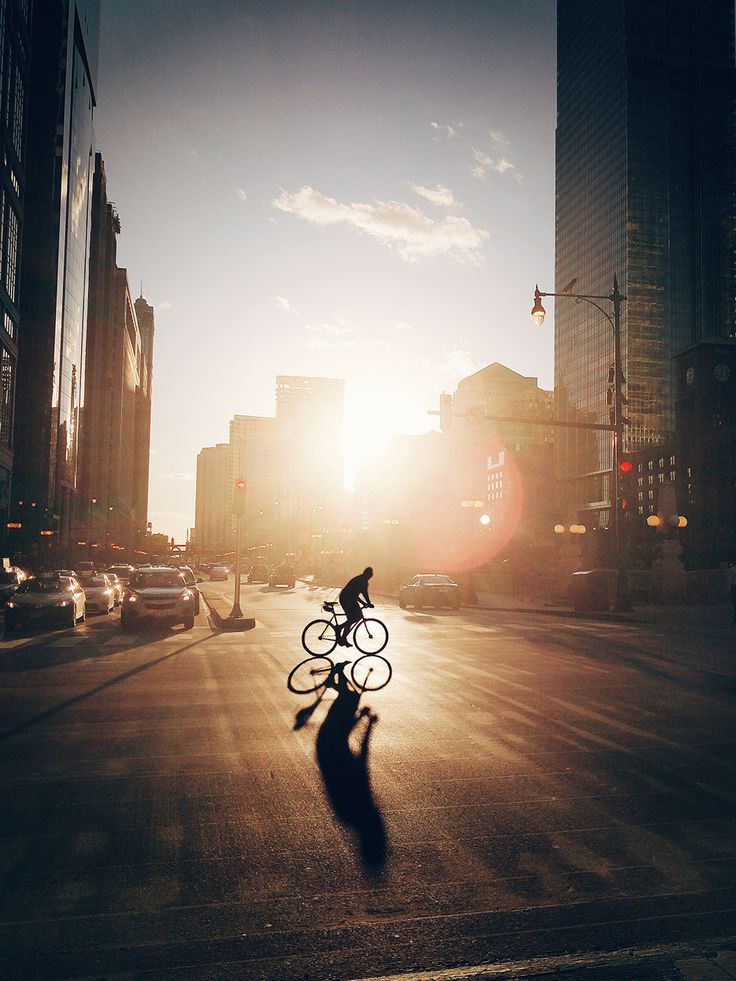 a person riding a bike down a street next to tall buildings and traffic lights at sunset