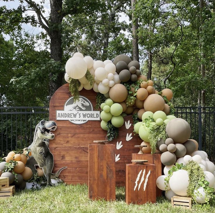 a dog sitting in front of a wooden sign with balloons and greenery on it