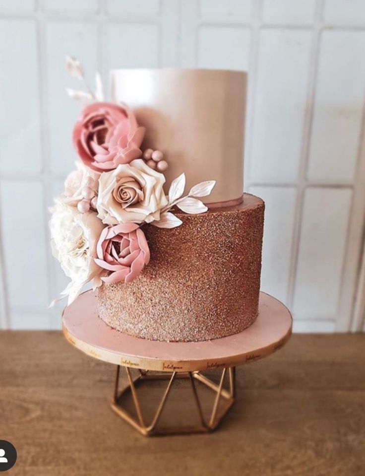 a three tiered cake with pink and white flowers on top, sitting on a stand