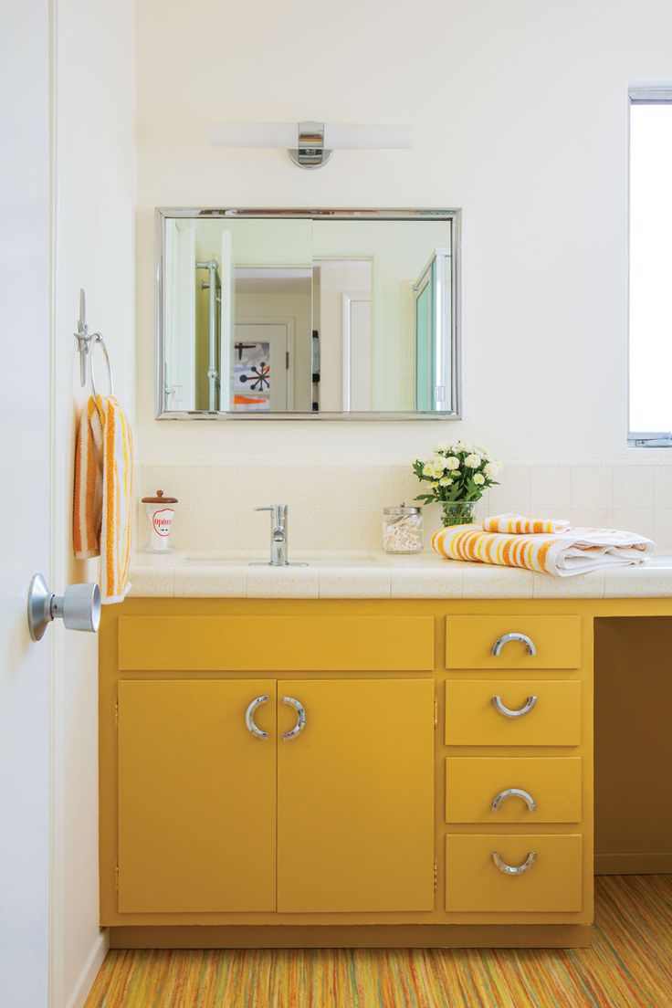 a bathroom with yellow cabinets and white counter tops, an orange rug on the floor