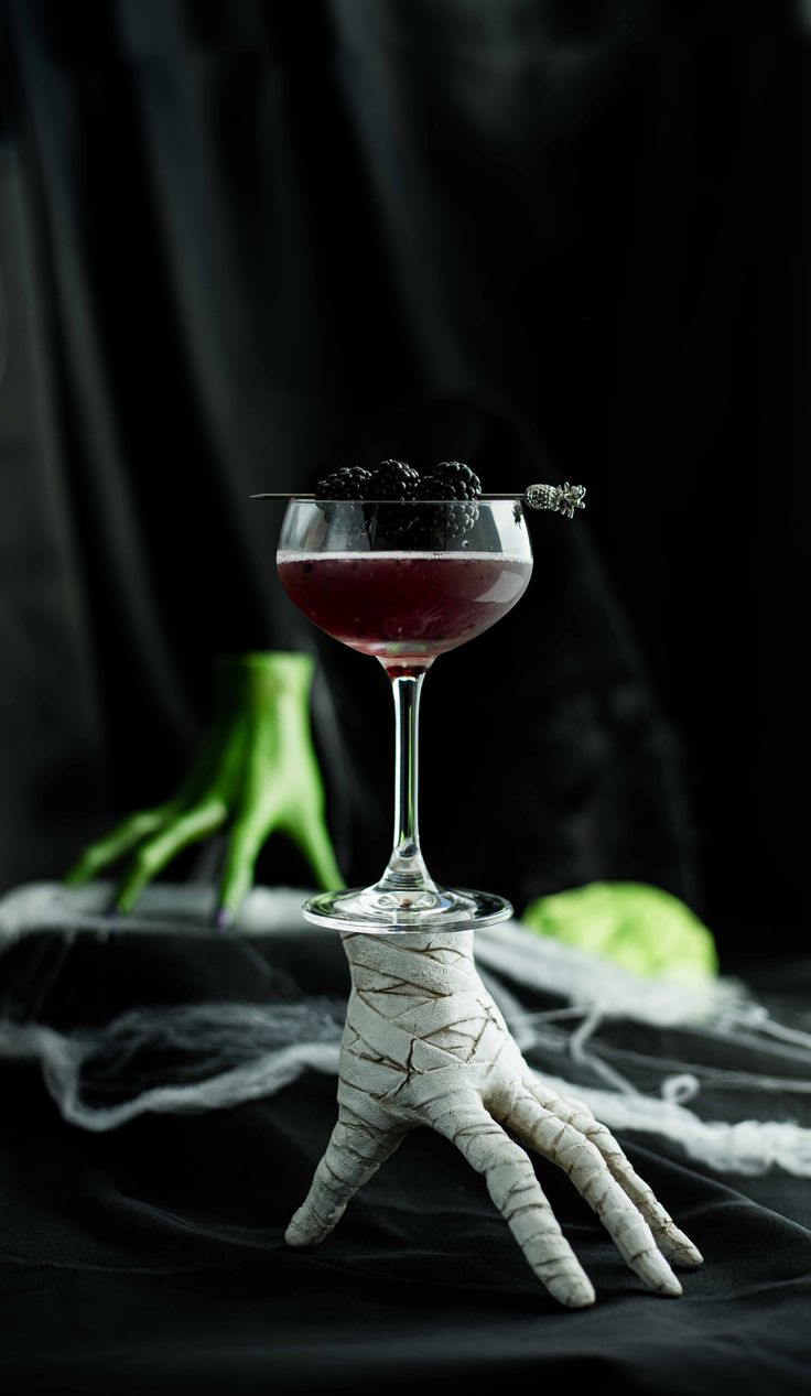 a halloween cocktail with garnish and spooky hands