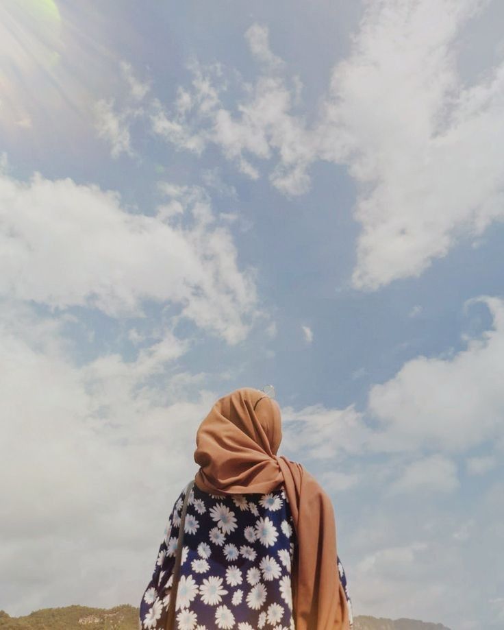 a woman walking on the beach carrying a surfboard under a blue sky with clouds