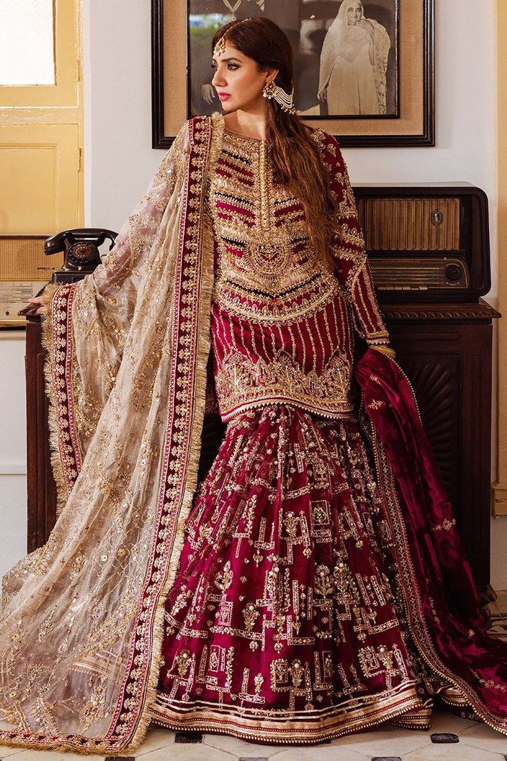 a woman in a red and gold bridal gown standing next to a painting on the wall