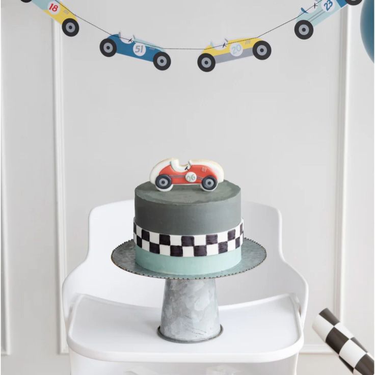 a cake with cars on it sitting on top of a white chair in front of a wall