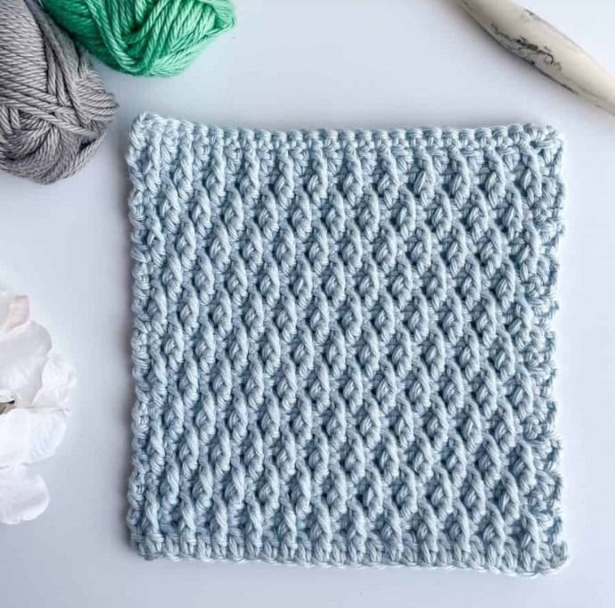 a crocheted dishcloth next to yarn and scissors