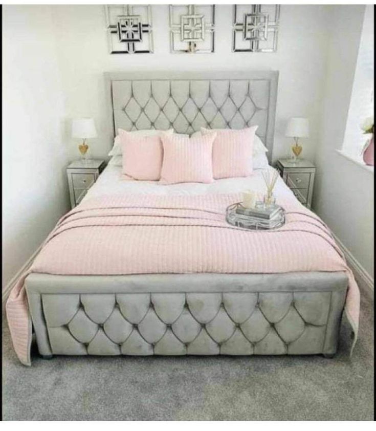 a white bed with pink pillows and some pictures on the wall above it, along with two nightstands