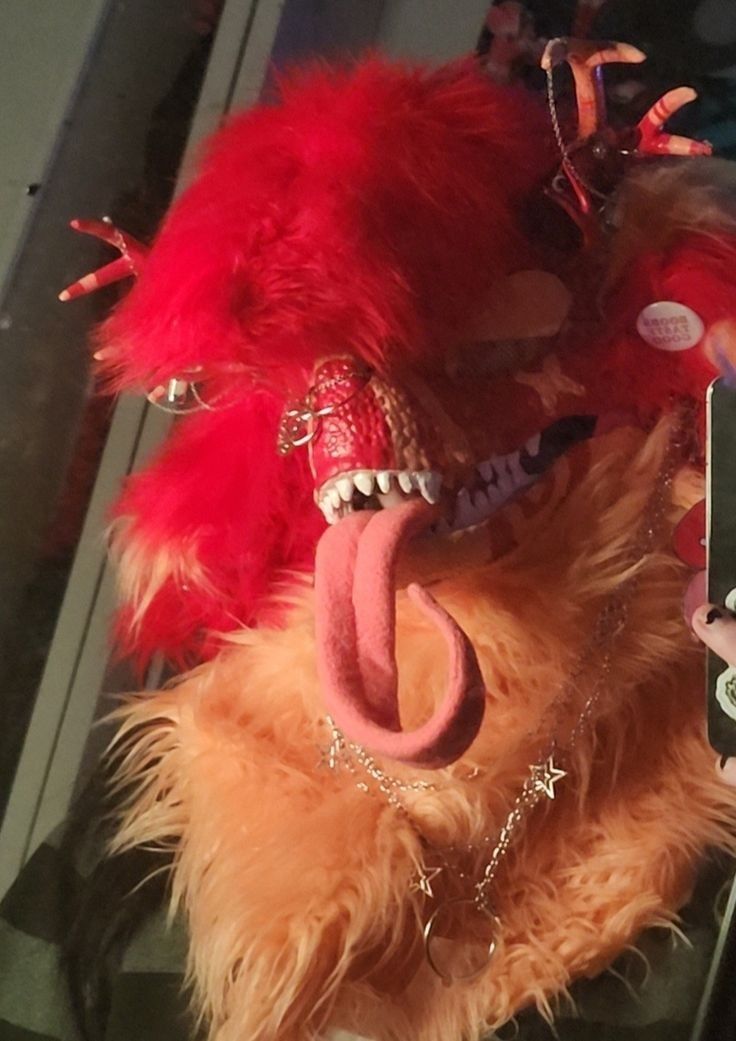 a stuffed animal has its mouth open and is wearing a red mask with chains around it's neck