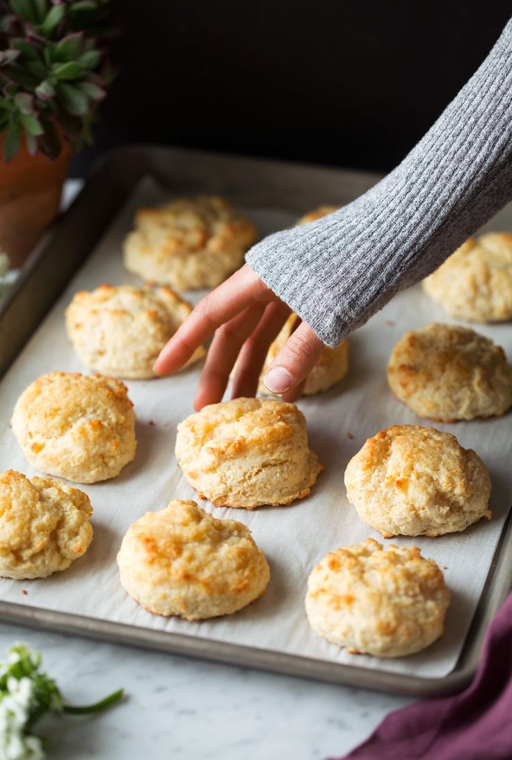 a person reaching for some biscuits on a baking sheet