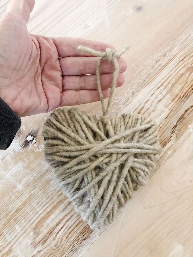 a hand holding a ball of yarn in the shape of a heart on a wooden table