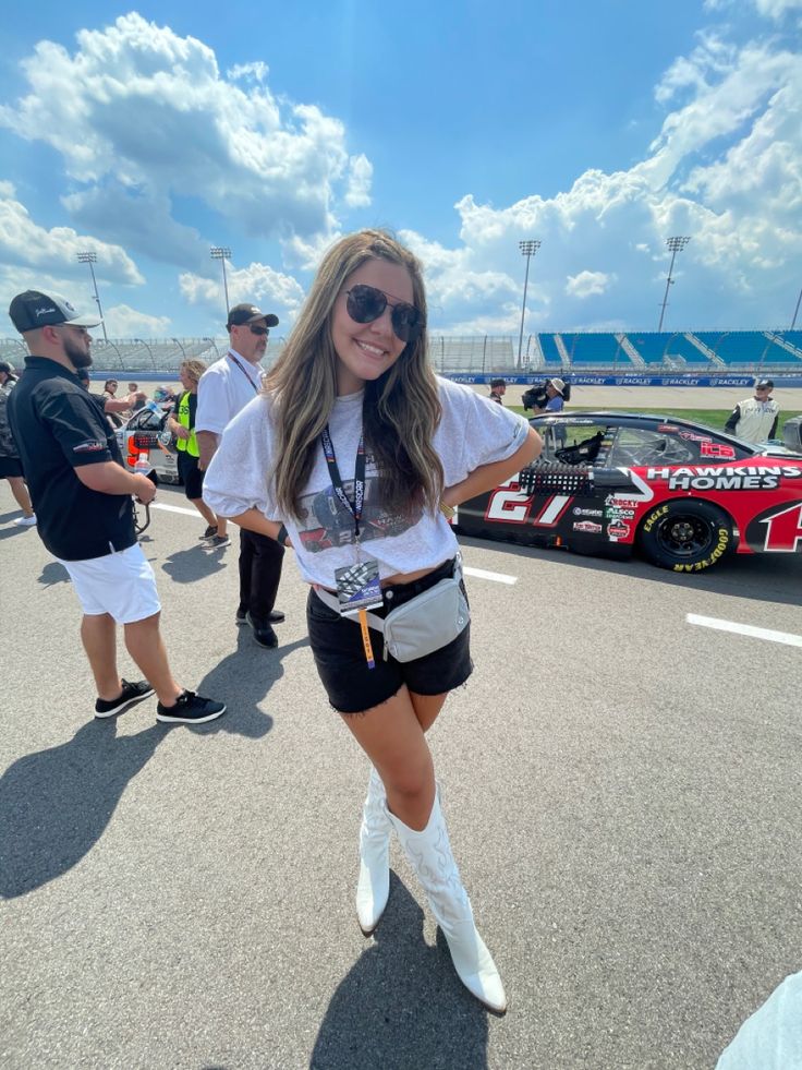 a woman in white shirt and black shorts standing next to a race car on the track