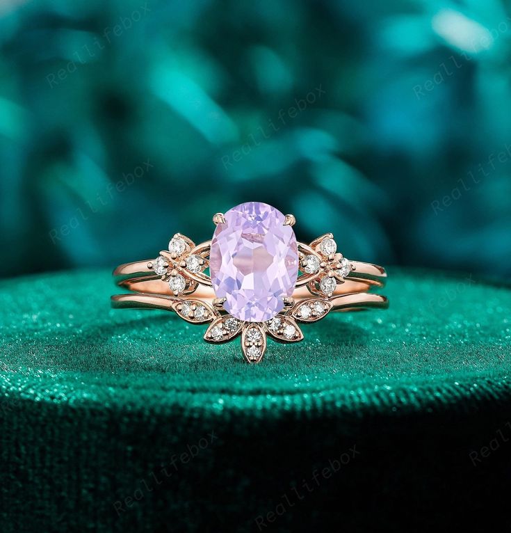 a pink ring sitting on top of a green velvet covered box with diamonds around it