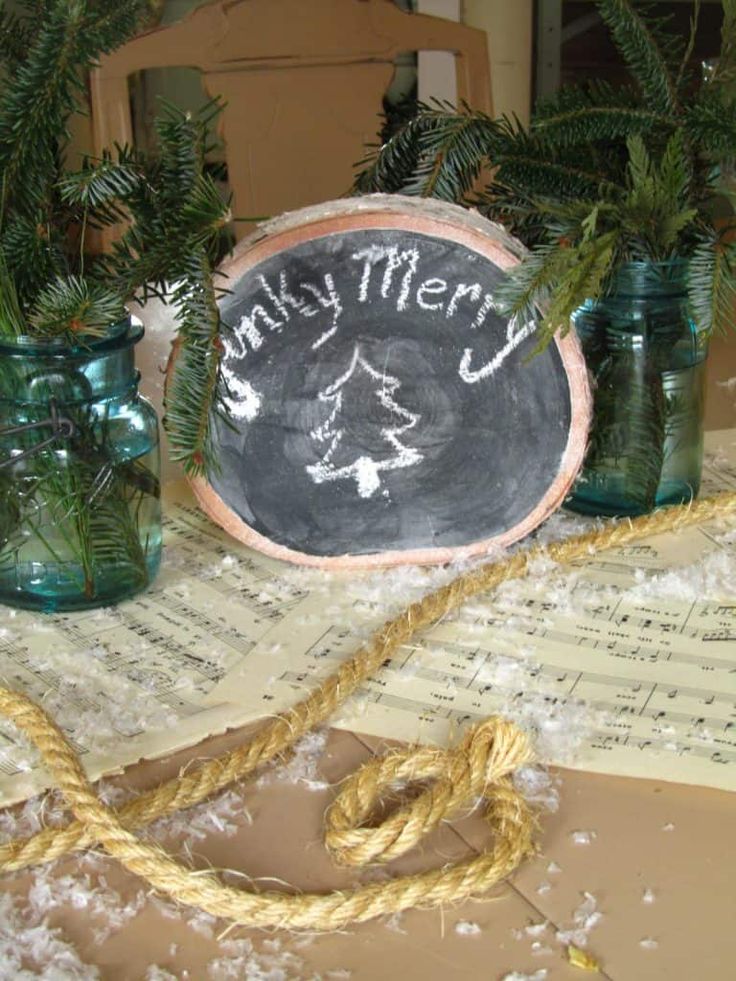 there is a chalkboard on the table with pine branches in mason jars next to it