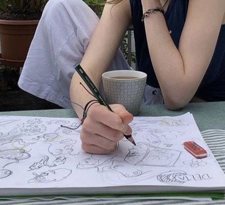 a woman sitting at a table writing on a piece of paper with a cup of coffee in front of her