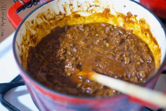 a red pot filled with food sitting on top of a stove next to a wooden spoon