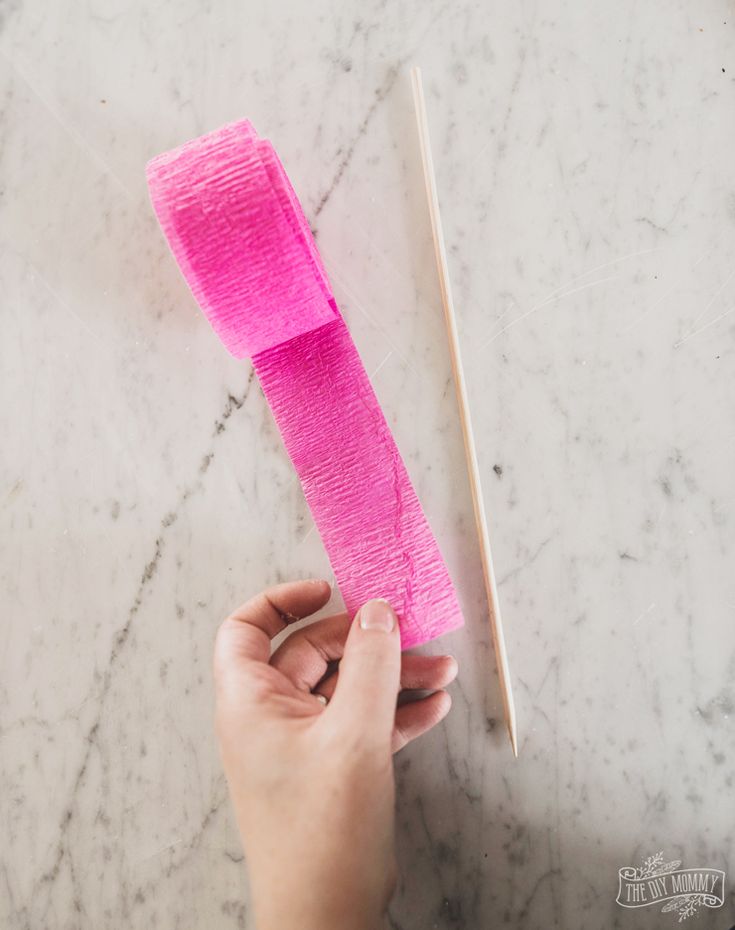 a person is holding a pink piece of cloth next to a pair of knitting needles