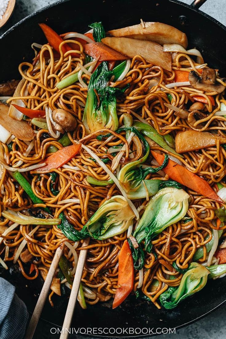 stir fried noodles with vegetables and chopsticks in a wok on the table