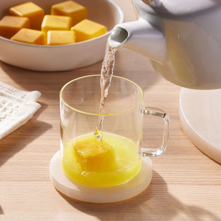 a pitcher pouring water into a glass cup with cubes of butter in the background