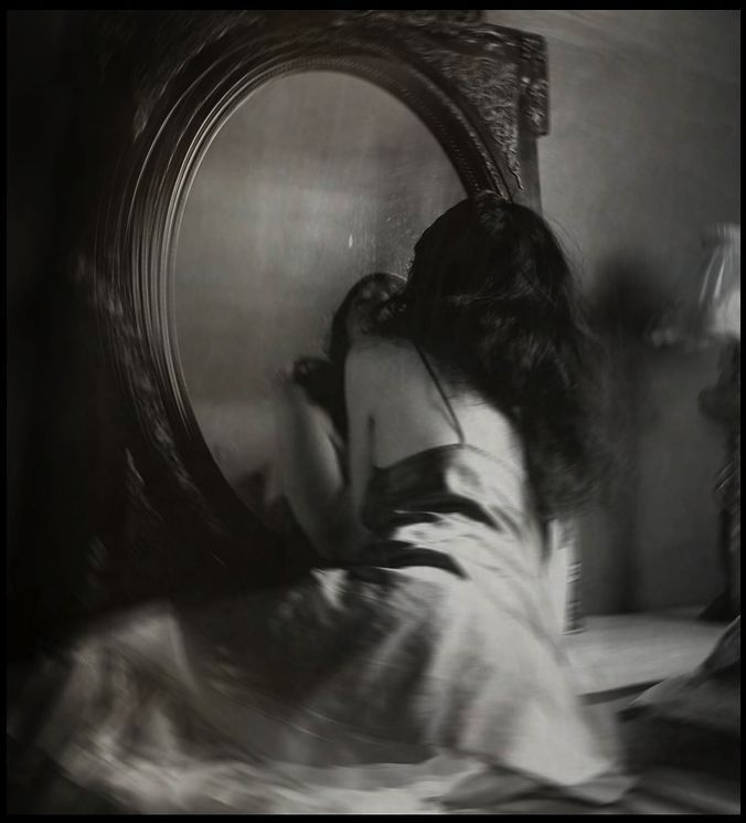 an old photo of a woman laying in bed looking at herself in the round mirror