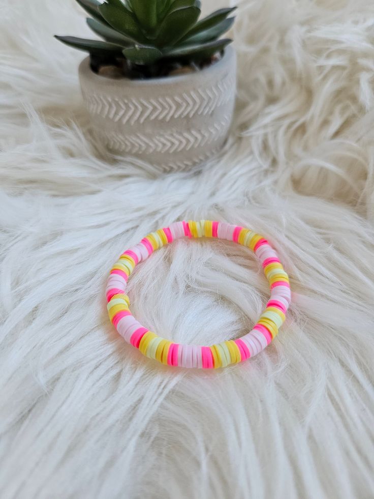 a pink and yellow beaded bracelet sitting next to a potted plant