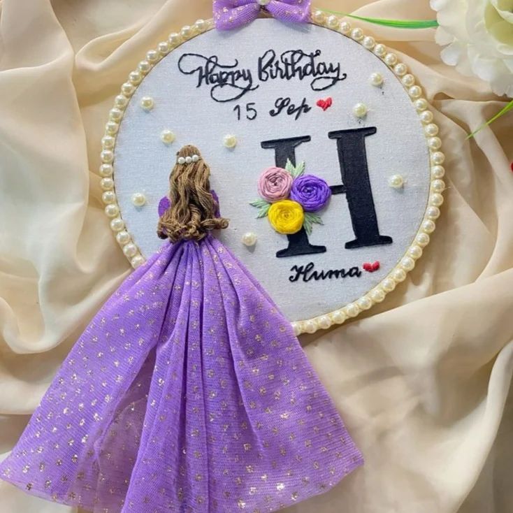 a birthday card with a purple dress and flowers on it, next to a cake