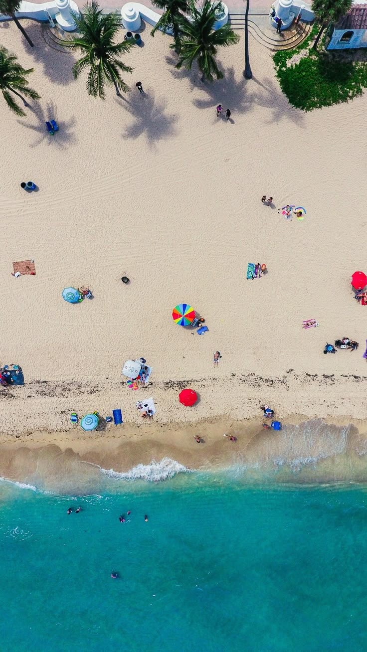 an aerial view of people relaxing on the beach and in the water, with umbrellas