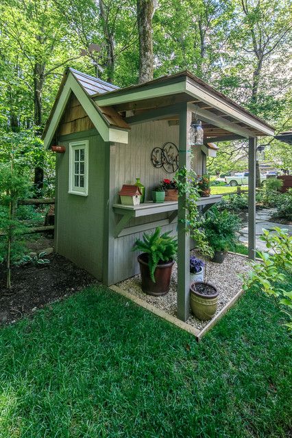 a small shed in the middle of a yard with potted plants and trees around it