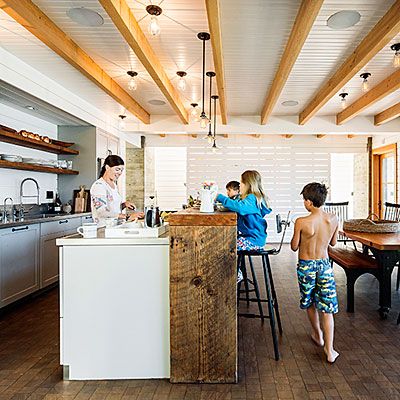 two children are standing in the kitchen with their backs turned towards the counter and chairs