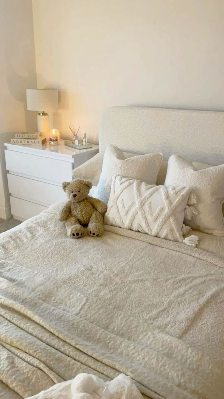 a teddy bear sitting on top of a bed in a room with white sheets and pillows