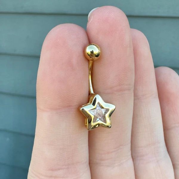 a person's hand holding a gold star belly ring