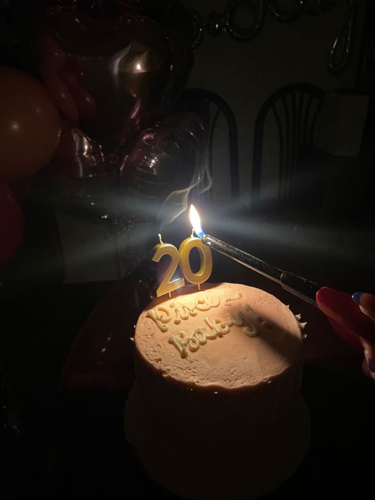 a birthday cake with the number twenty on it, lit by a candle and surrounded by balloons