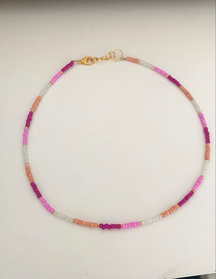 a pink and white beaded necklace with gold clasp on a table next to a mirror