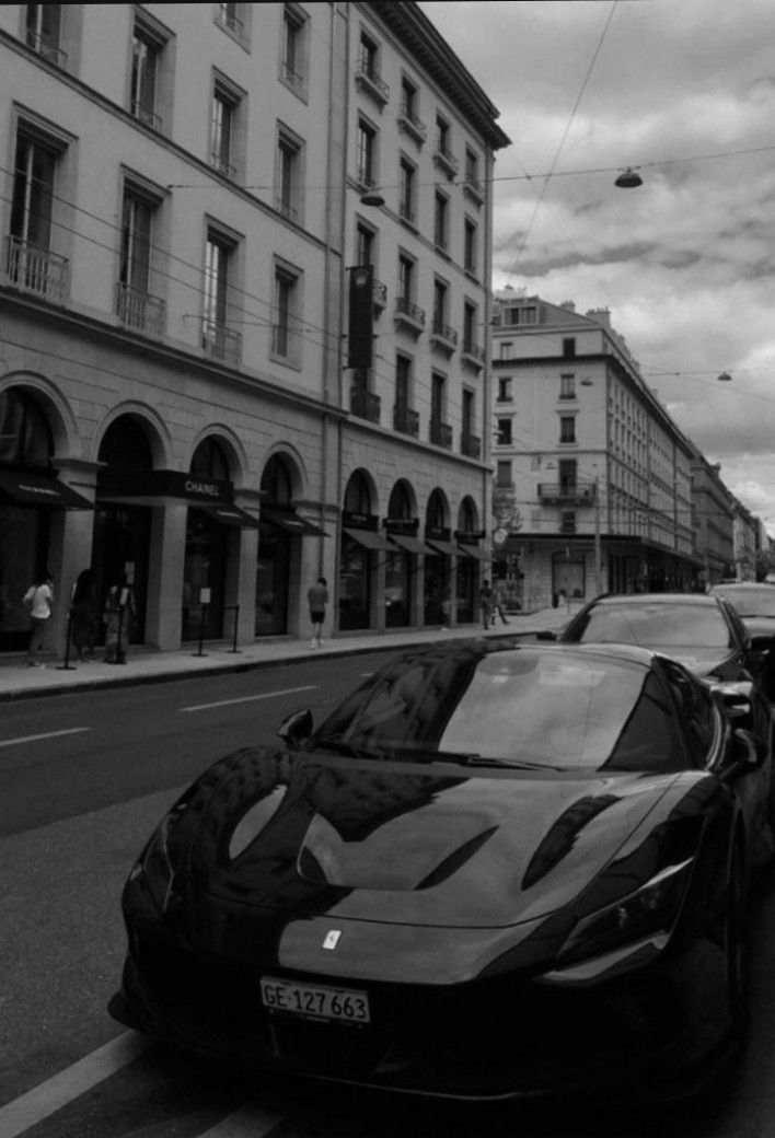 black and white photograph of cars parked on the side of the road in front of buildings