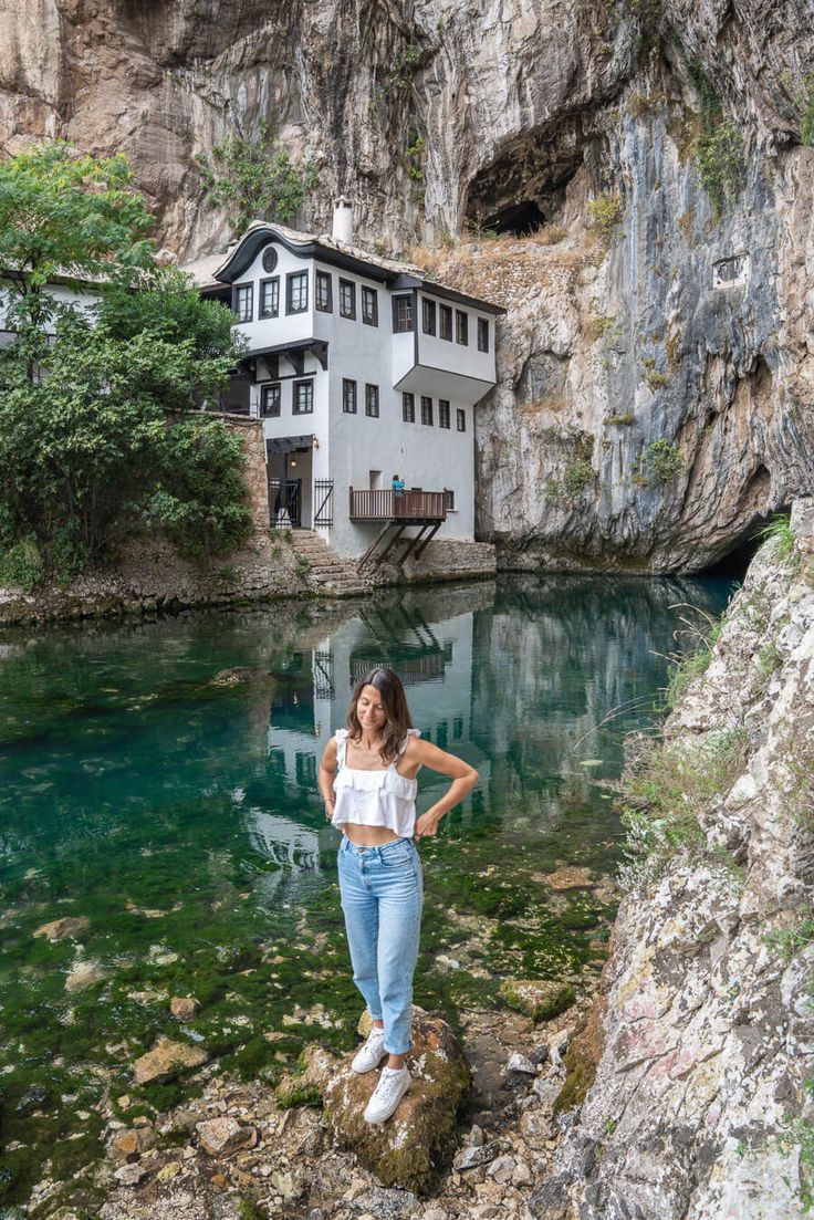 a woman standing on rocks in front of a house next to a body of water