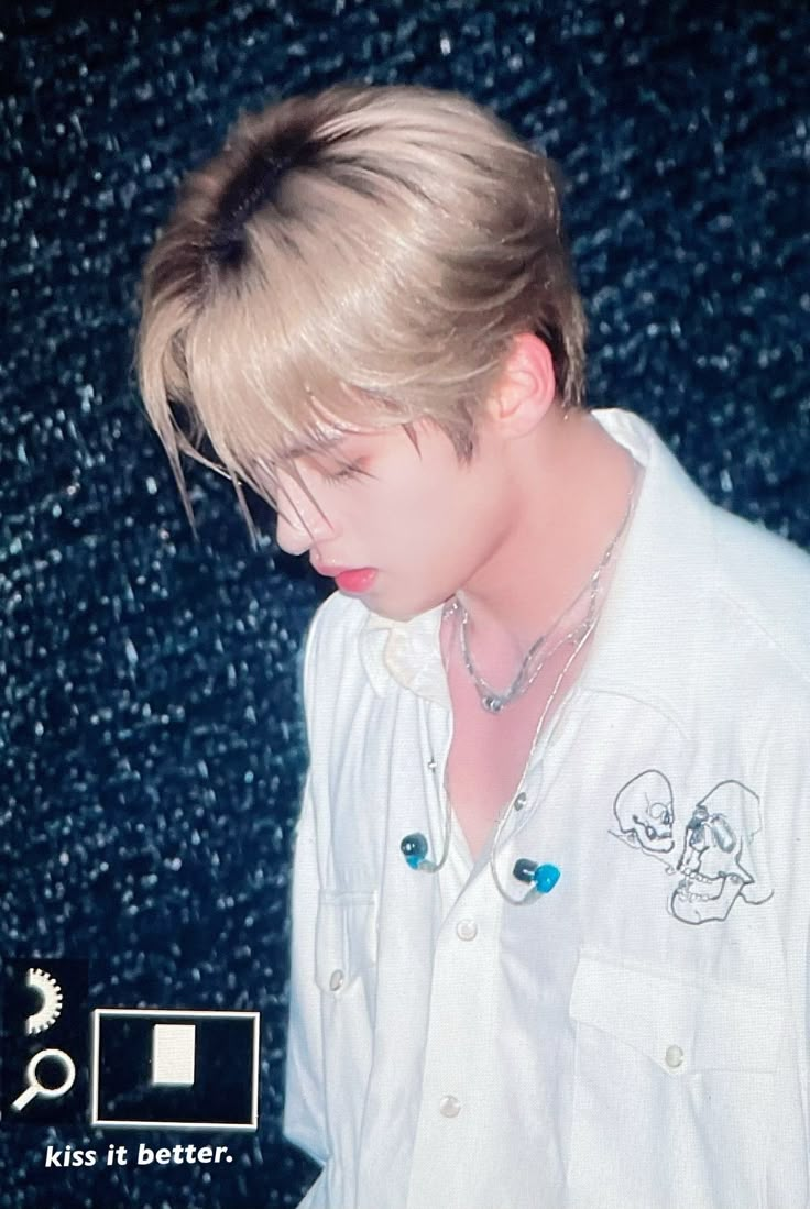 a young man with blonde hair wearing a white shirt and silver necklace, standing in front of a black background