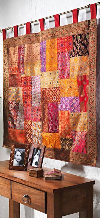 a wooden table topped with an orange and red patchwork quilt hanging on the wall