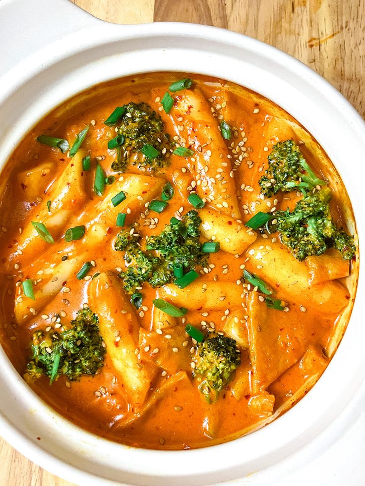 a white bowl filled with broccoli and dumpling in sauce on top of a wooden table