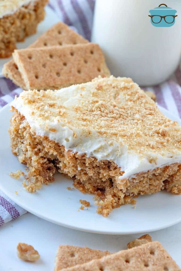 a piece of cake with white frosting on a plate next to crackers and a glass of milk