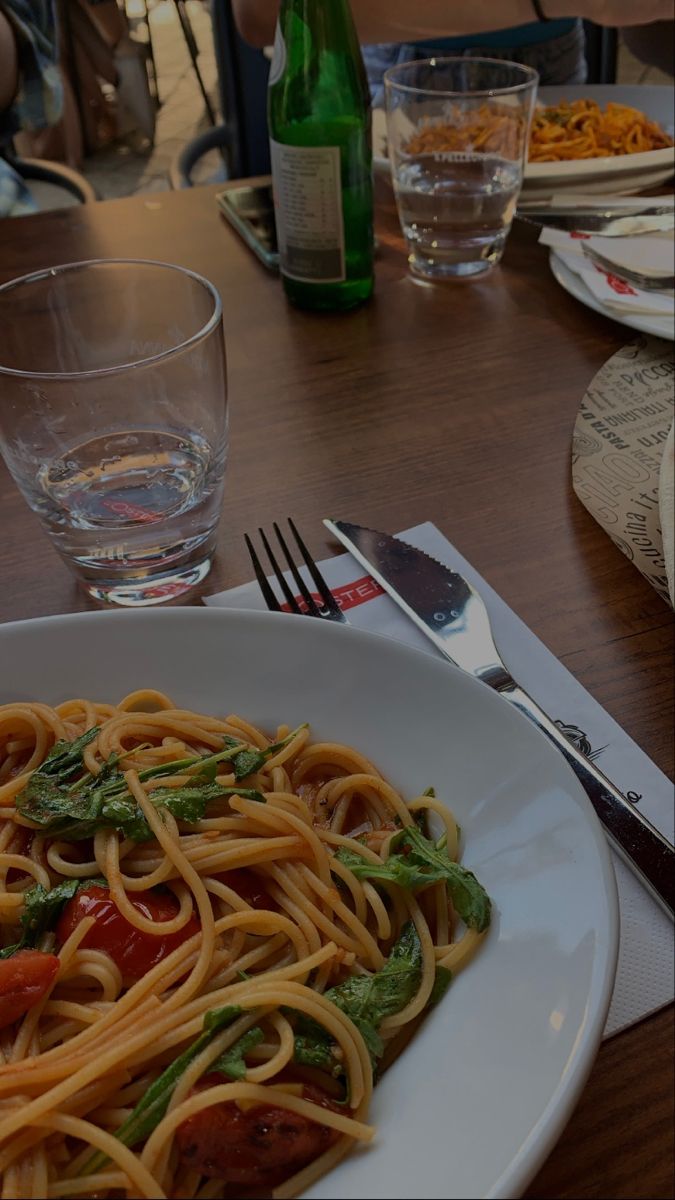 a plate of pasta with tomatoes and spinach on it next to a glass of water