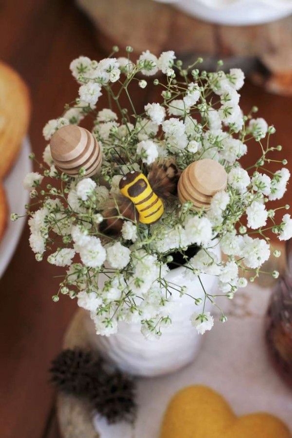 a vase filled with white flowers and bees on top of a table next to cookies